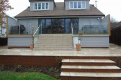 Cladded bespoke terrace with brick dwarf wall. Oak trim with infinity glass & natural stone steps & patio area